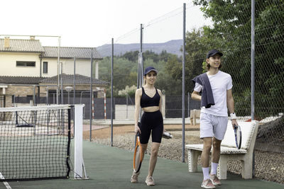 Young cute couple casualy walking arriving happily to a tennis court to practise exercise 