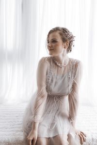 Beautiful young woman sitting on bed at bedroom