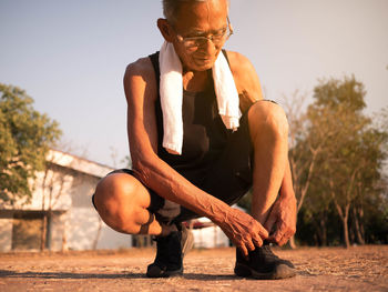 Man tying shoelace while crouching on land against sky