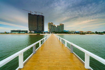 Pier over sea by buildings against sky