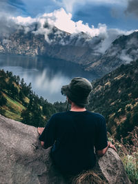 Rear view of man sitting on mountain against sky