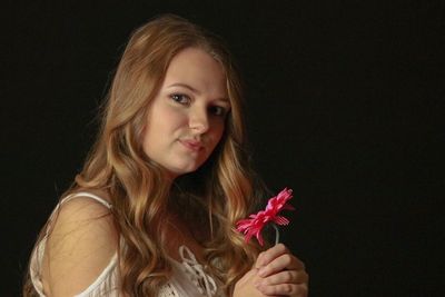 Portrait of beautiful young woman holding flower against black background