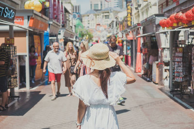 Rear view of woman wearing hat standing on street in city