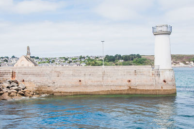 Lighthouse on building by sea against sky