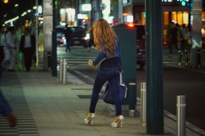 Rear view of woman walking on sidewalk in city