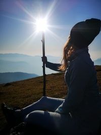 Side view of woman sitting on mountain against sky