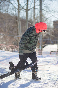 Full length of man with snowboard walking on snow covered field