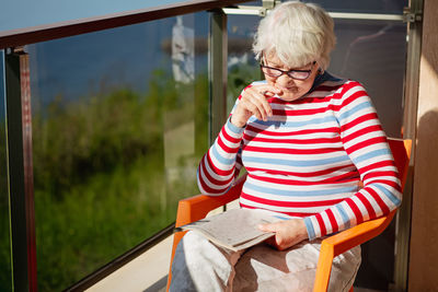 Senior woman in glasses sitting on balcony near the sea