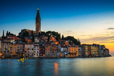 Buildings by sea against sky during sunset