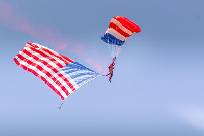 Low angle view of person paragliding with american flag against clear blue sky