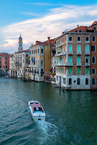 Boat in canal amidst buildings in city against sky. gran canal, venice italy.