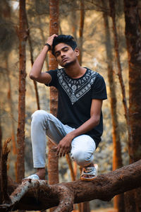 Full length of young man sitting on tree trunk