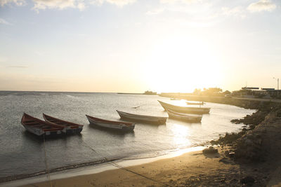 Boats moored on beach against sky during sunset