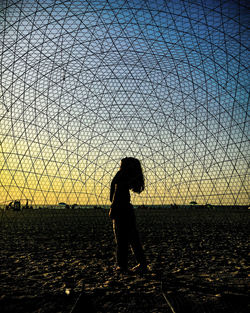 Silhouette woman standing on beach against sky during sunset