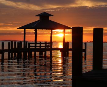 Silhouette built structure by sea against sky during sunset