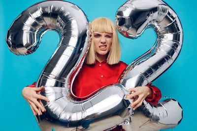 Young woman with balloons standing against blue background