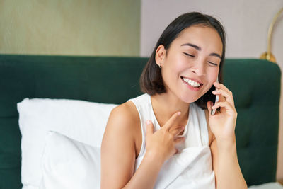 Portrait of young woman looking away while sitting on bed at home