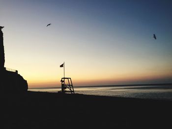 Silhouette birds flying over sea against sky
