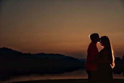 Silhouette couple standing against orange sky during sunset