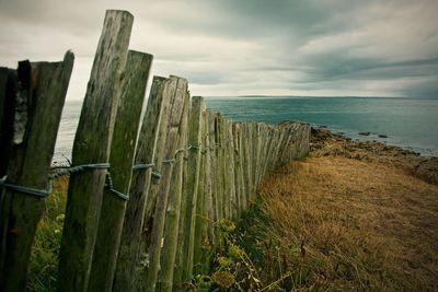 Wooden fence on beach against cloudy sky