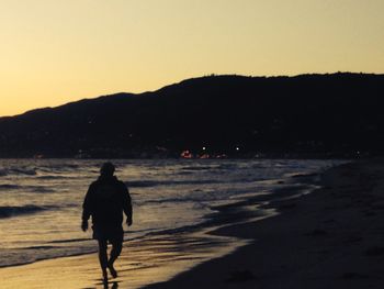 Silhouette man walking on beach against clear sky during sunset