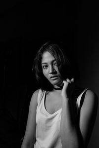 Portrait of young woman sitting against black background