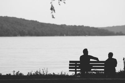 Rear view of couple sitting on lake against clear sky