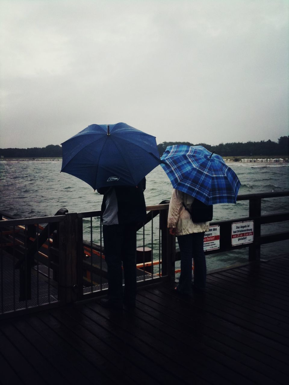 rear view, water, lifestyles, full length, leisure activity, sea, sky, pier, standing, person, tranquility, tranquil scene, relaxation, men, casual clothing, sitting, railing, nature