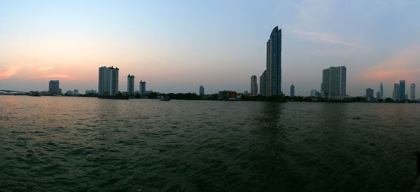 Sea by buildings against sky during sunset