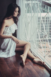 Young woman looking away while sitting by window at home