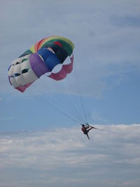 Low angle view of woman paragliding against cloudy sky