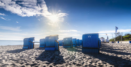Hooded beach chairs on sand against sky on sunny day
