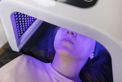 Blue led light mask for face skin therapy, care. young girl gets problem skin treatment, lying on