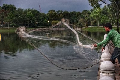 Full length of boy fishing in river against sky