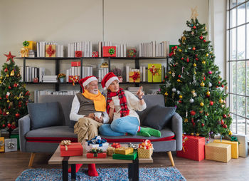 Senior caucasian couple relax on sofa holding hot drink looking view outside window on christmas day