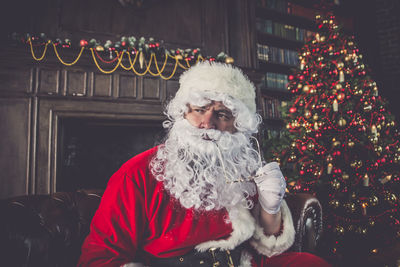 Man wearing santa claus costume sitting by christmas tree on sofa at home