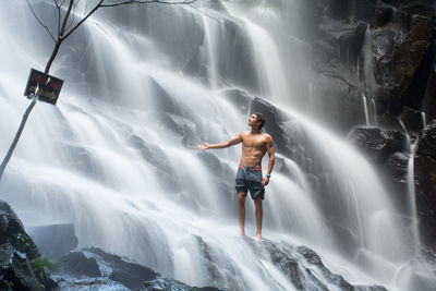 Shirtless man standing by waterfall