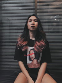 Portrait of beautiful young woman sitting against shutter