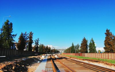 Railroad tracks amidst trees against clear blue sky