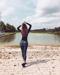 Full length rear view of woman walking on footpath by lake against sky