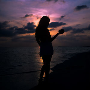 Silhouette woman standing on beach against sky during sunset