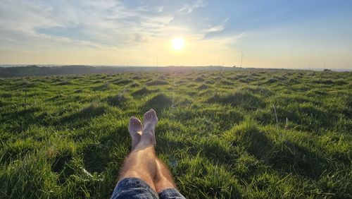 Rear view of man standing on field against sky during sunset