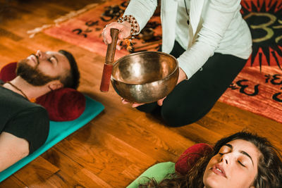 Low section of therapist playing rin gong by couple while performing music therapy at spa