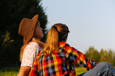 Back view of mother and daughter sitting on meadow and looking at green field. friendship love