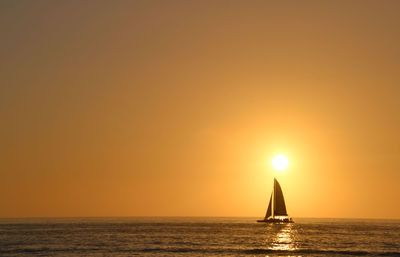 Sailboat sailing on sea against clear sky during sunset