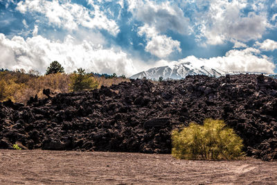 Scenic view of rock formations and mountain against cloudy sky during sunny day