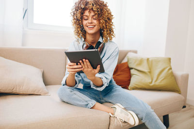 Young woman using phone while sitting on sofa at home