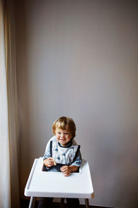 Cute boy sitting on table against wall