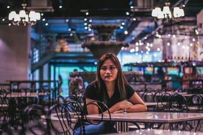 Portrait of smiling woman sitting on illuminated restaurant at night