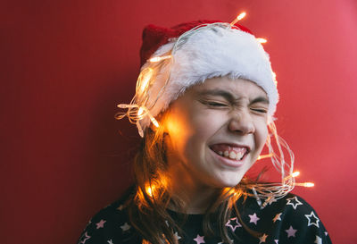 Girl with illuminated string light against red wall